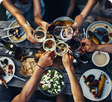 Looking down on peoples&#39; arms as the toast over a table of food